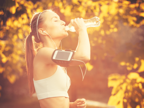 Fit fall essentials - girl running, listening music and drinking water in a park