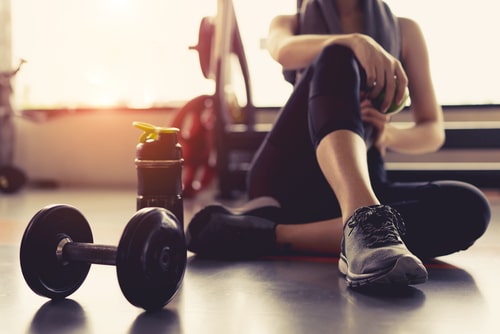 A woman sitting on the floor in a gym with dumbbells.
