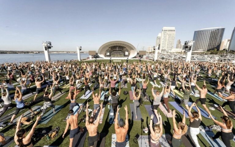 A large group of people doing yoga in front of a city.