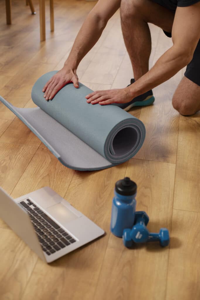A man is laying down a yoga mat on a wooden floor.