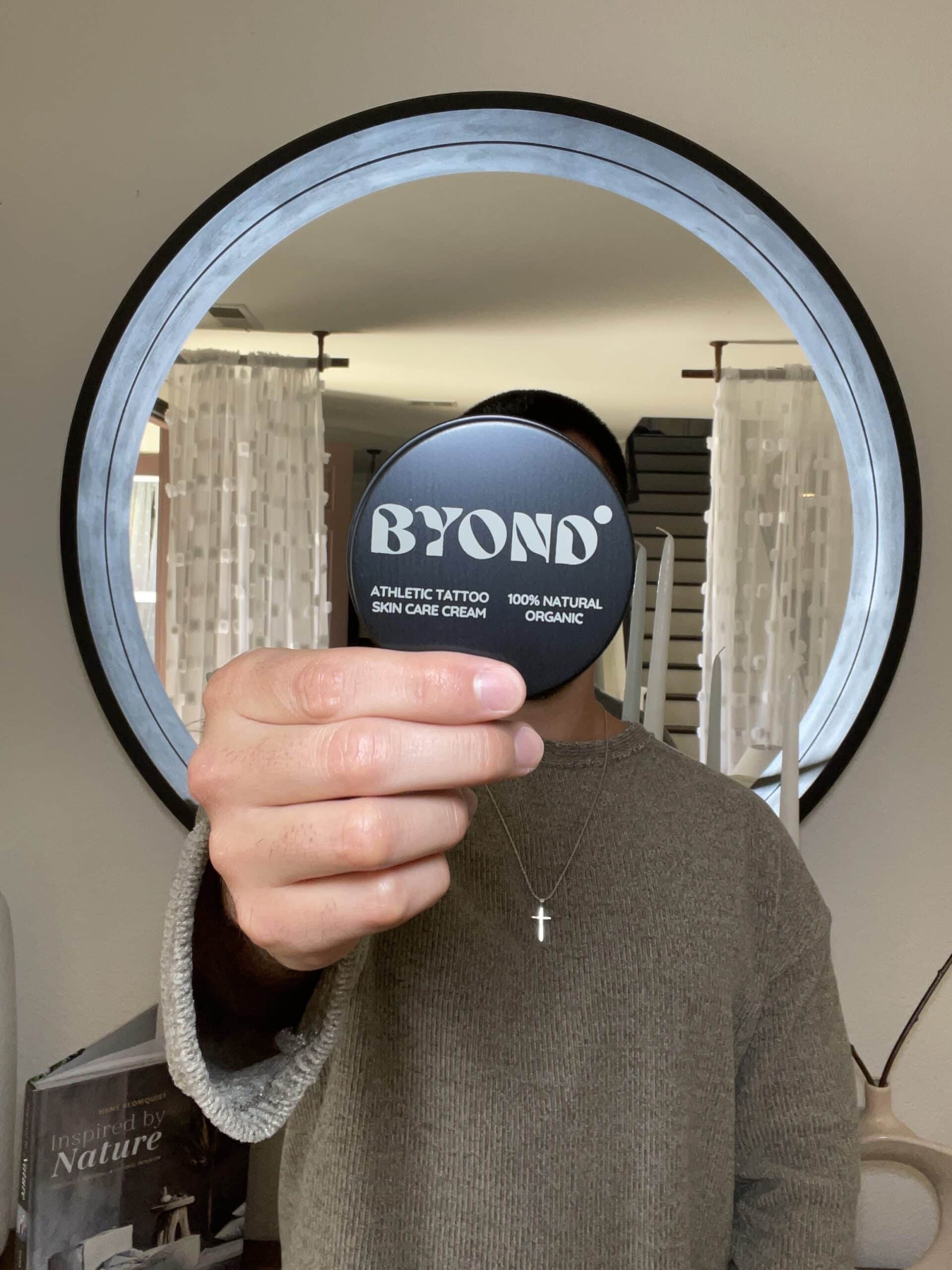 Person holding up a skincare product in front of their face, reflecting in a round mirror.
