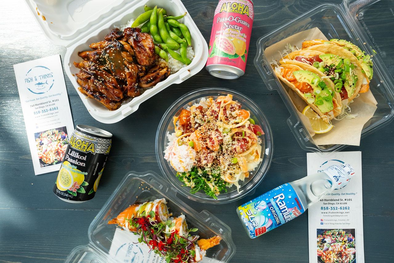 A variety of takeout dishes and drinks spread on a wooden table with menus and business cards.
