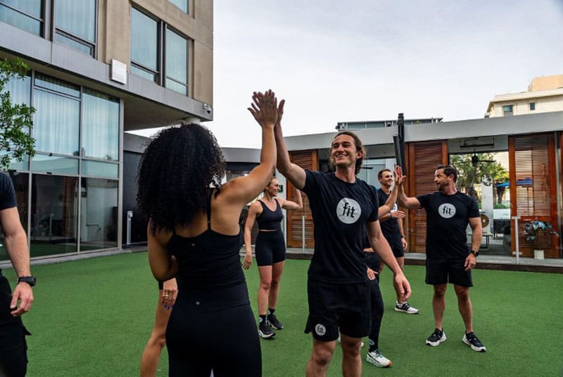 Group of people in athletic wear high-five each other on a grassy outdoor area.