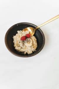 A bowl of oatmeal topped with banana slices, berries and chia seeds, with a gold spoon on the rim.